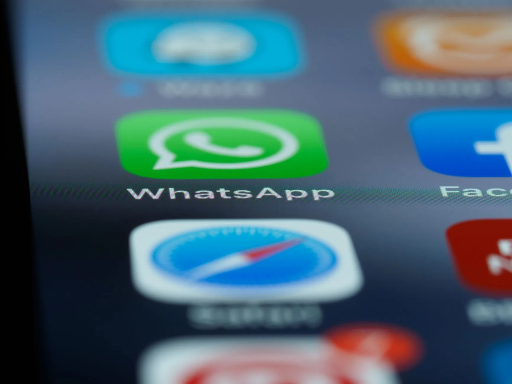 Celular exibindo conversa de atendimento no WhatsApp apoiado sobre uma mesa de trabalho com notebook